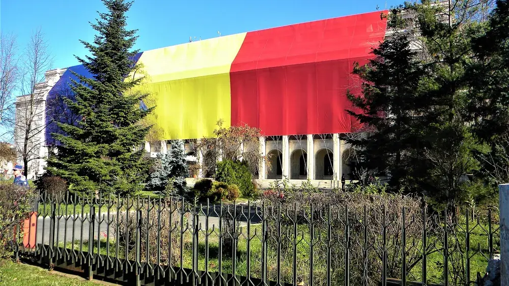 Palatul Victoria, sediul Guvernului României, acoperit cu un drapel tricolor uriaș, văzut printre brazi